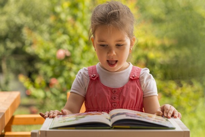 Outdoor portrait of an adorable young little girl reading a book in the garden